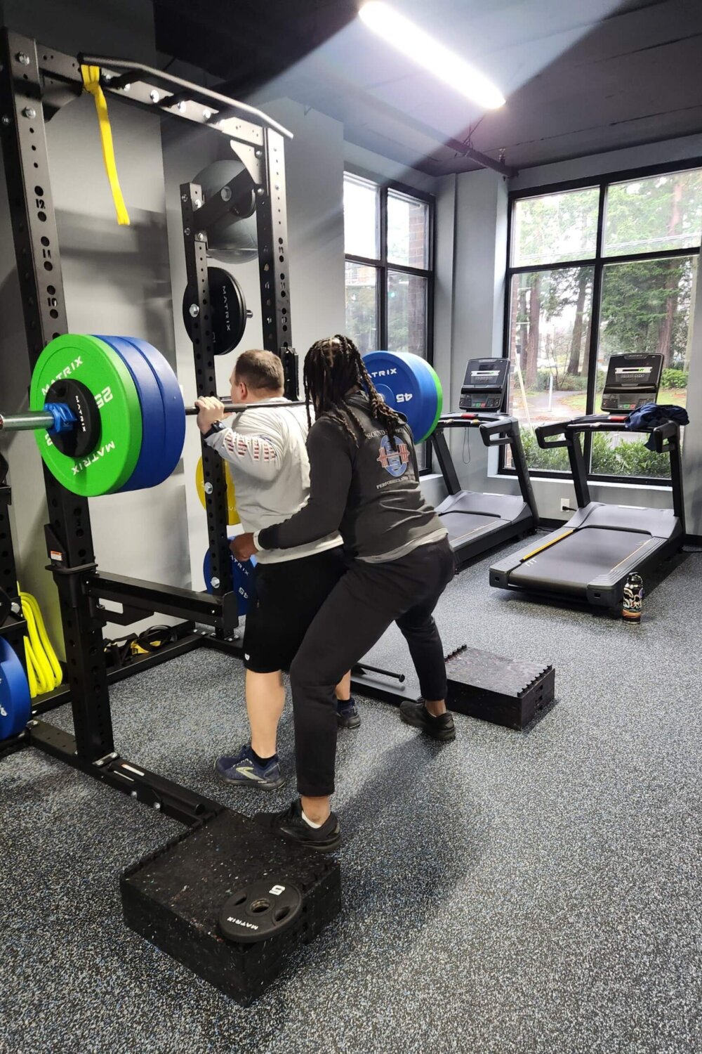 A coach spotting a client during a barbell squat at Sound Sports.