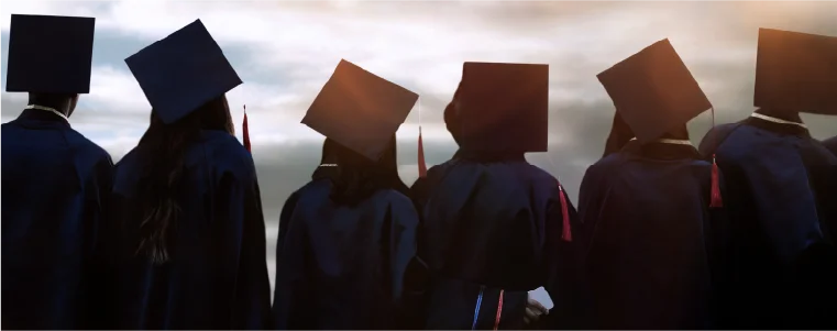 Graduates wearing caps and gowns at sunset.